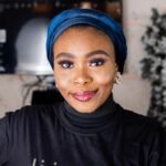 Vibrant portrait of a smiling woman indoors wearing a blue turban and stylish black turtleneck.